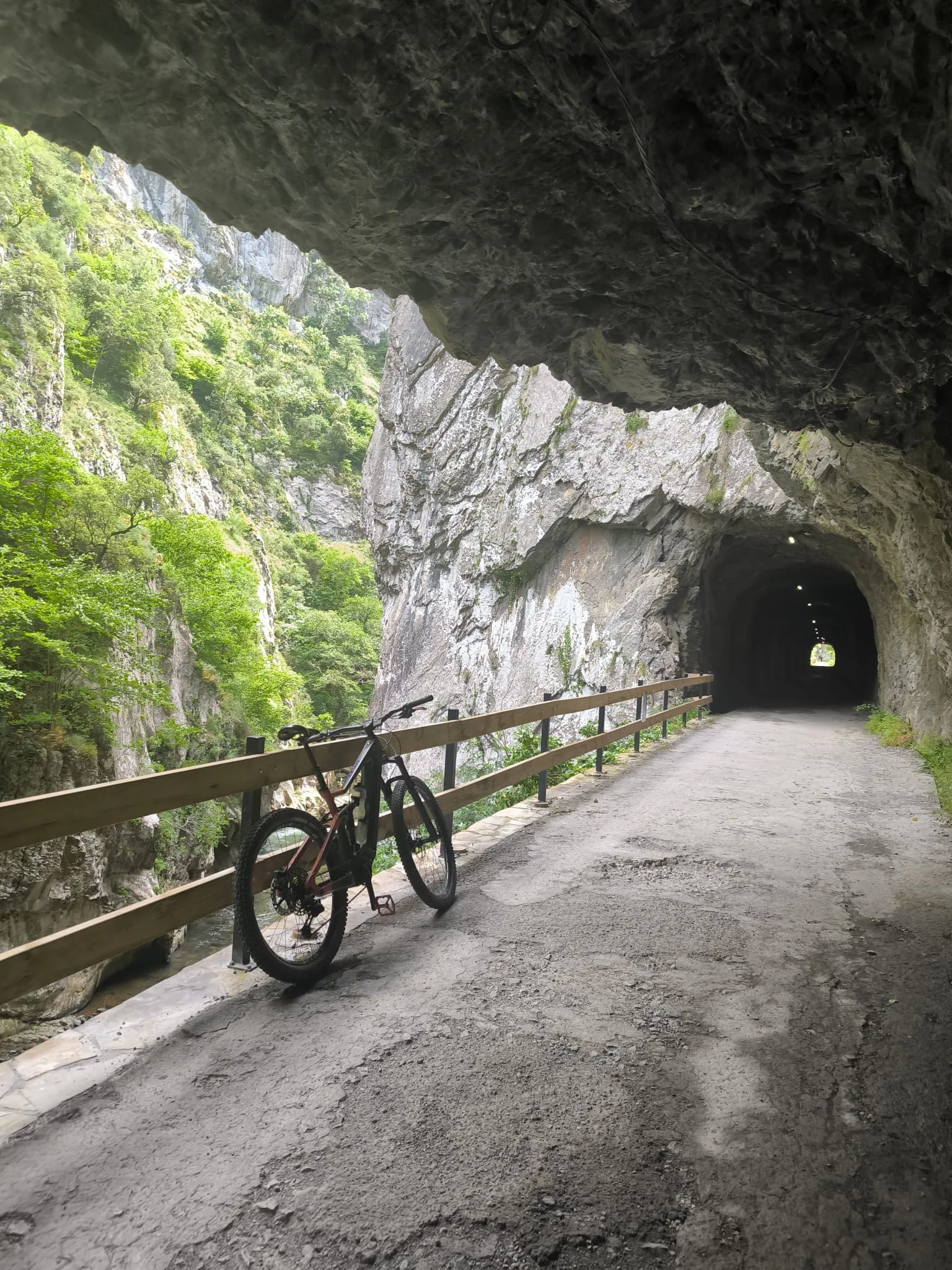 Túnel de roca en la Senda del Oso con bicicleta apoyada en la barandilla junto al río